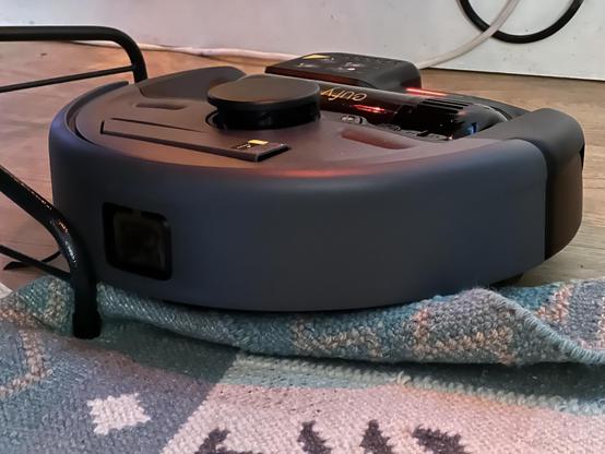 A robot vacuum cleaner hopelessly stranded on a thin, bunched up rug.