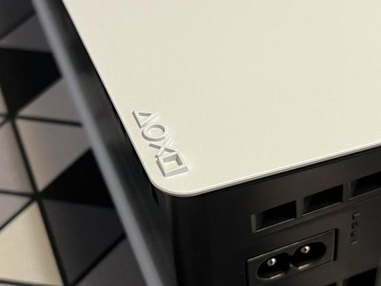 The bottom right corner of a PS5 Slim, just showing the power socket and fan ports. The sacred symbols - Triangle, Circle, Cross, Square - are embossed on the white side plate.