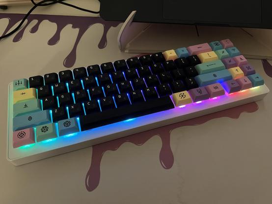 A WhiteFox eclipse mechanical keyboard with colourful pastel modifier keycaps and black alphas. It’s sat atop a white deskmat with a pink and purple paint drip pattern. A jagged dark water mark bisects the mat.