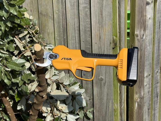 A large yellow electric pruning tool, stuck fast in a wooden branch and jutting out horizontally.