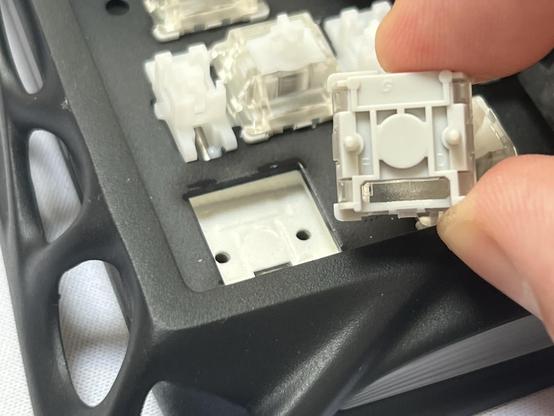 Fingers holding a switch removed from a keyboard. It has no electrical contacts, relying instead on the magnetic “Hall Effect.”