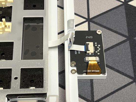 The fragile cable in question snaking out from under a PCB mounted in the bottom of the keyboard and into an LCD daughter board mounted in the top shell.