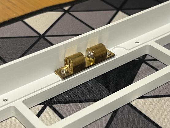 A contrasting brass cabinet catch screwed into the white top shell of a keyboard. It uses two spring loaded ball bearings to grip a nub on the other side.