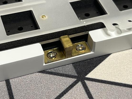 A brass nub screwed into the bottom shell of a keyboard, designed to fit snugly into the spring loaded catch. Very obviously just a regular, cheap cabinet door catch you might use around the home.