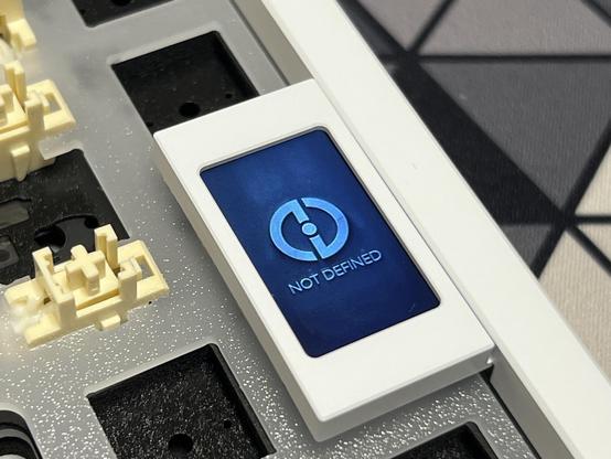 A tiny LCD screen in an unpopulated mechanical keyboard showing a “Not Defined” slogan under a logo splash screen.
