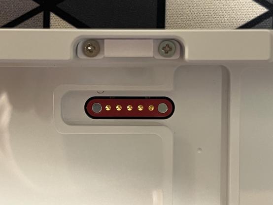 The bottom shell of the keyboard revealing a red rounded rectangle shape with two magnets at opposite ends and five copper pogo pin receptacles spaced evenly in the middle. A tiny little MagSafe sorta!