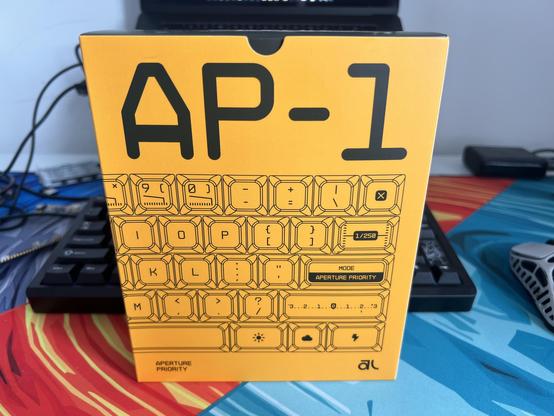 A PC-game sized yellow box stood upright on a desk. It has line art of keycaps and a huge AP-1 title.