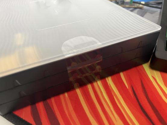 Side on view of three black plastic trays held together with a clear sticker. A semi translucent lid caps off the stack.
