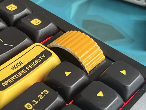 The edge of a mechanical keyboard with a 3D-printed and painted fake jog wheel added in place of the normal “badge” detail.
