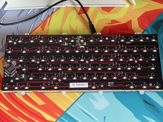 The PCB of a mechanical keyboard laying upturned on a desk. Many LEDs and various other components are visible but no sockets or soldered switches!
