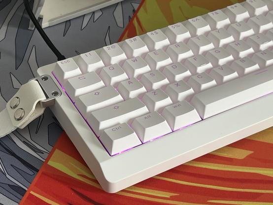 A white mechanical keyboard with white shine through keycaps and a white strap attached to the left-hand edge.