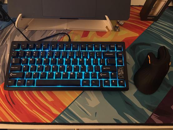 A black 75% mechanical keyboard lit up ice blue and sat on a deskmat with diagonal swipes of colour.