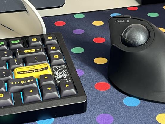 A ProtoArc wireless trackball mouse sat next to a mechanical keyboard on a colourful dotty desk mat.