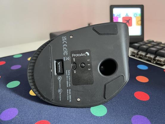 The bottom of a trackball mouse. It’s got quite a large footprint and noticeably rubber pads in lieu of glides. Two screws are visible.