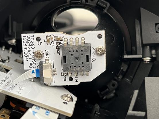 A small white PCB with a large PAW3212 optical sensor mounted through it. A ribbon cable to the main PCB snakes away to the left.