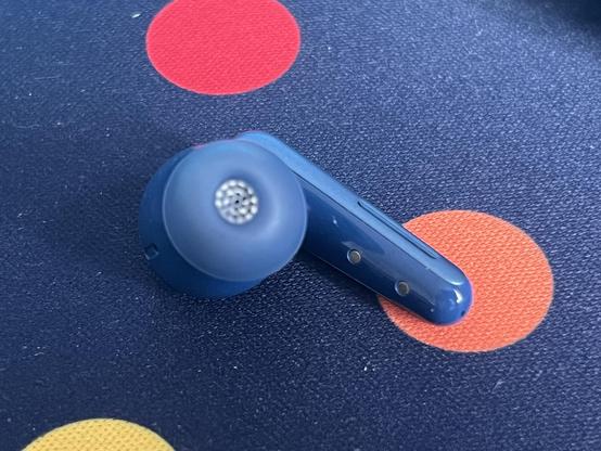 A single earbud laid on a blue forty deskmat.