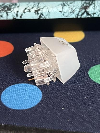 A keycap stuck to a clear switch which has separated into its top and bottom halves.