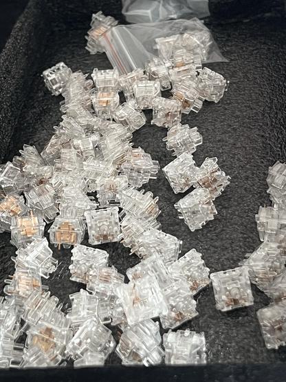 A scattering of transparent keyboard switches with visible copper contacts sat in the foam insert of the keyboard packaging.