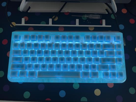 A keyboard lit up ice blue with blue ceramic keycaps, above it sits an aluminium trim piece from around the F keys, a screwdriver and the screws that secured it.