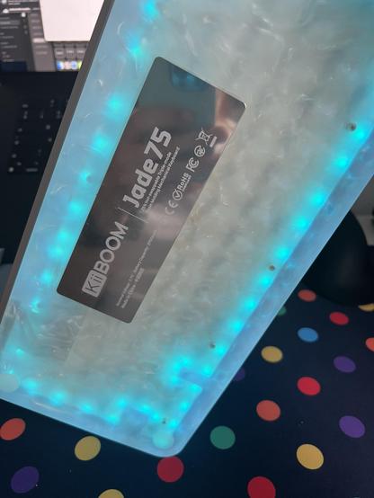 A view through the bottom of a swirled resin keyboard showing a ring of blue LEDs around the edge and a slightly wonky reflective aluminium badge glued to the bottom.