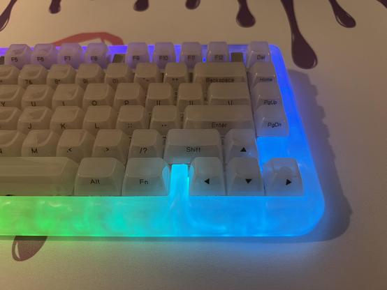 A mechanical keyboard lit up purple green and blue around the edges, revealing a swirly resin texture in the case.