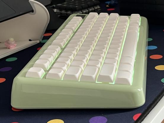 A side view of a high gloss plastic keyboard with not quite fully pushed down blank white keycaps. They are a uniform, low profile with a gentle spherical scoop.