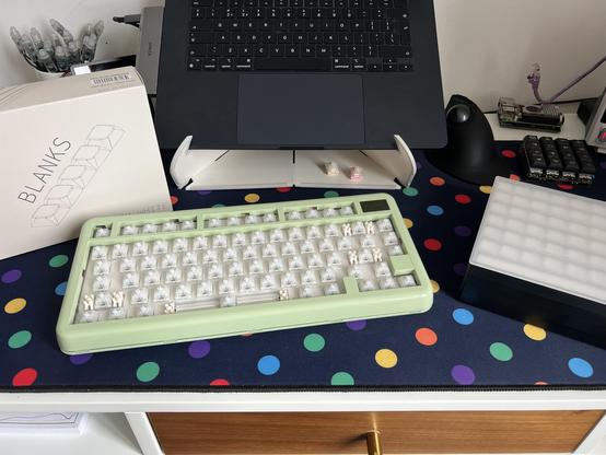 A gloss plastic green keyboard sitting between an empty PBS Blanks box and a neat stack of keycap trays. The keyboard has no keycaps populated.