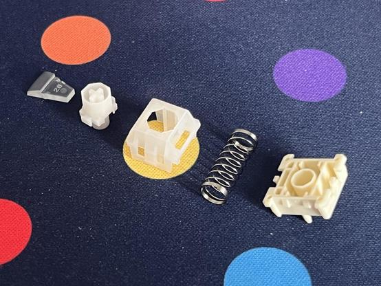 A disassembled mechanical keyboard switch, its parts arrayed out on a dotty deskmat.