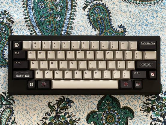 A black keyboard with very tragic off white and black keycaps featuring overly busy legends with no real tonal consistency.
