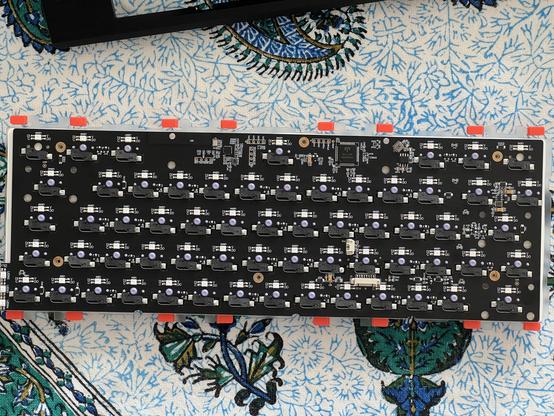 The underside of a keyboard PCB showing mostly the array of hot swap switch sockets. Around the edge are sixteen bright orange protrusions coming from the plate- little cantilever mounting arms with silicone dampers on each.