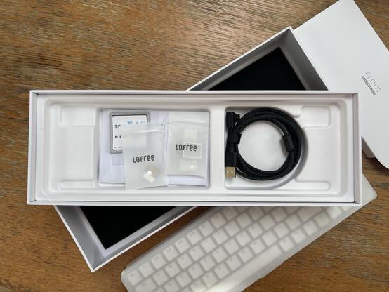 Underneath a low profile keyboard a neatly coiled right-angle USB Type-C cable and small bags with alternate keycaps and a 2.4GHz USB dongle.