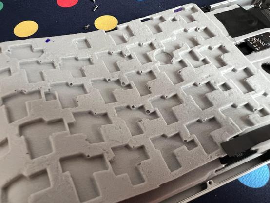 A sheet of grey keyboard damping foam with a series of impressions shaped to accommodate  switch hot swap sockets and their adjacent LEDs. It’s very rough and coarsely manufactured with what seem like popped bubbles dotting some corners.