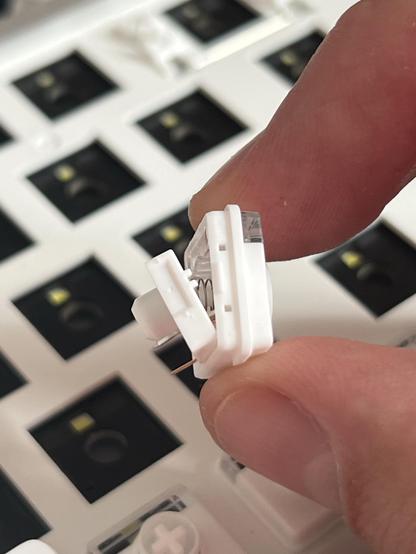 A white low profile Lofree x Kailh “Cloud Series” switch, split apart with the internal spring showing.