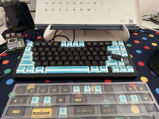 A keyboard with a mix of crazed ceramic and low profile black plastic keycaps. It’s in the process of swapping from one set to the other. A tray in the foreground also has a mix of the two styles.