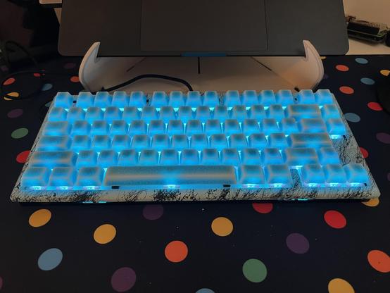 Establishing shot showing the full mechanical keyboard with its blue illuminated ceramic keycaps and marble effect replacement top shell. It blends relatively well and looks at least somewhat intentional.
