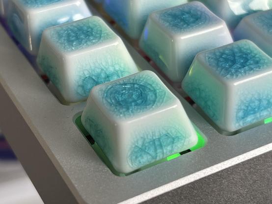 A closeup of the ESC key in a mechanical keyboard. It has a ceramic glaze, crazed into a pattern of concentric circles like a laminated window hit with a stone.