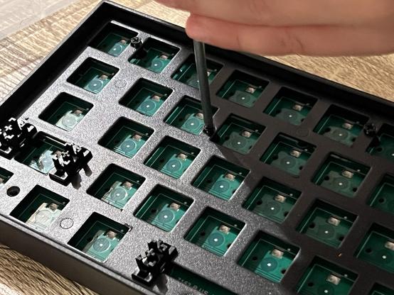 A small hand unscrewing a screw from a the plate in the top of a black mechanical keyboard.