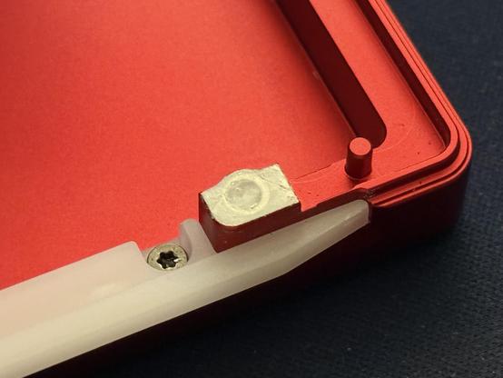A plastic light diffuser screwed onto a red aluminium keyboard button shell. The screw is in an unfortunate place, blocking some light that would otherwise have filled out the bar where it overlaps the case.