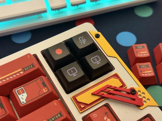 Four black keycaps with video streaming related icons looking a little out of place on a white, yellow and red keyboard.