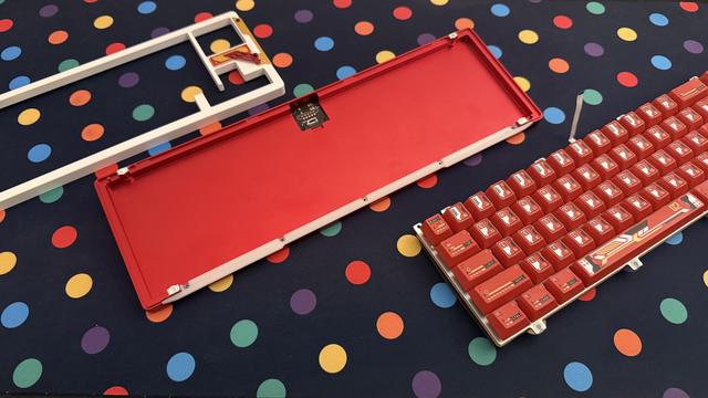The top shell, bottom shell and keybed of a red and white mechanical keyboard, laid out upon a dotty deskmat.