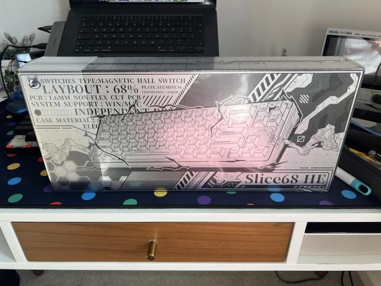 A shiny silver box atop a desk. It features monochrome art of a keyboard with mecha styled background details.