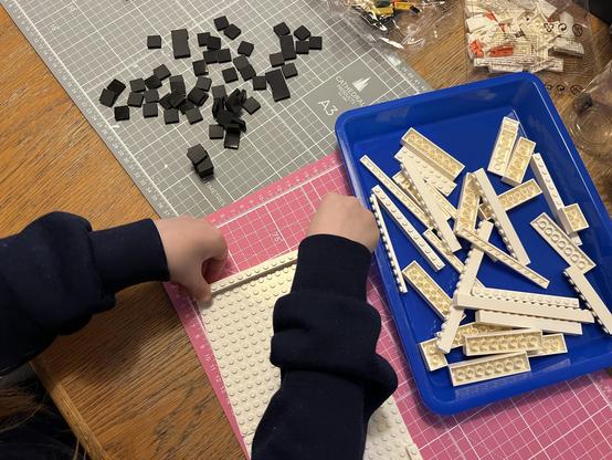 Small hands pushing white LEGO-like bricks down onto a white baseplate.