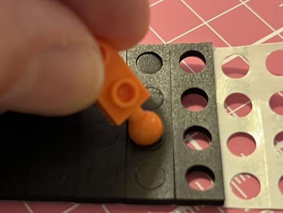 A little orange ball joint being pushed down onto the pre-cut holes in a foam pad.