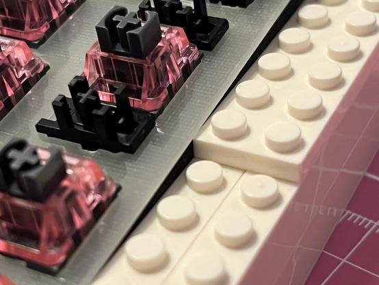 An FR4 plate with keyboard switches installed, resting on the outer edge of a brick enclosure.