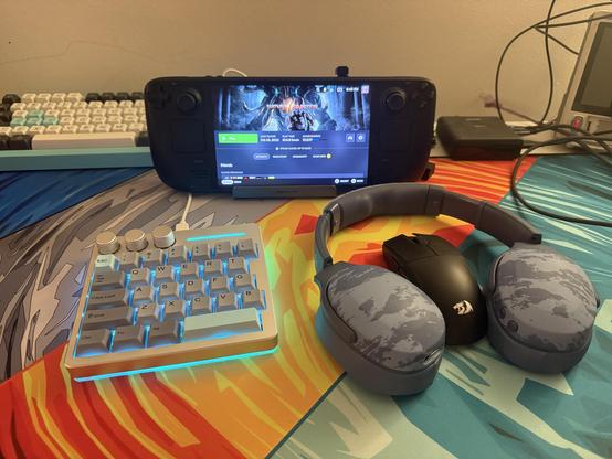 A Steam Deck sat in an unofficial dock with a weird half-a-keyboard - the KiiBOOM Cybrix29 - in front of it on the left, joined by a Redragon mouse and a pair of camo Skullcandy Crusher Evo headphones.