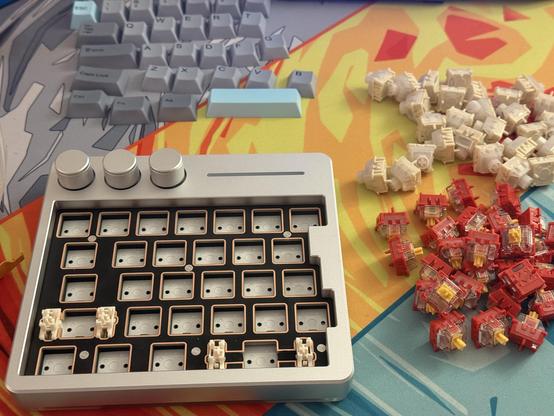 The Cybrix 29 with the keycaps and switches removed. Two piles of 29 switches sit next to it- the red/orange stock ones and the beige Wuque Flux.