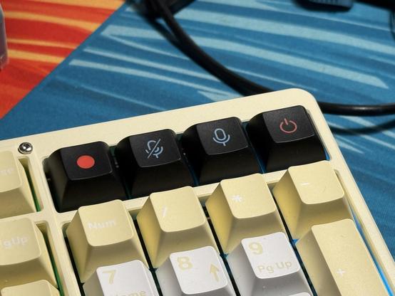 Four black icon keycaps for record, mute, unmute and power set in a row in a yellow keyboard.