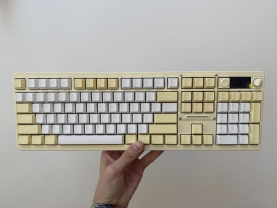 A hand holding up a hefty aluminium full-size keyboard in yellow and white.