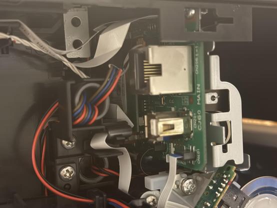 A closeup of the mainboard inside a printer. A wireless module is tucked tricky behind an Ethernet and USB port.