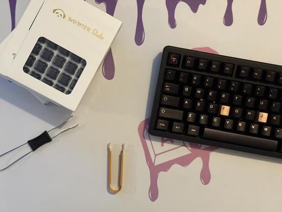 A stack of 35 quantity switch boxes sat next to a black keyboard with black and gold keycaps. A keycap puller and switch puller sit nearby.